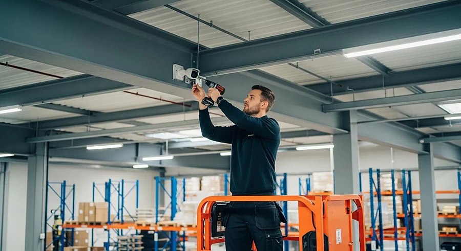 Installer fitting a CCTV camera to a warehouse ceiling beam